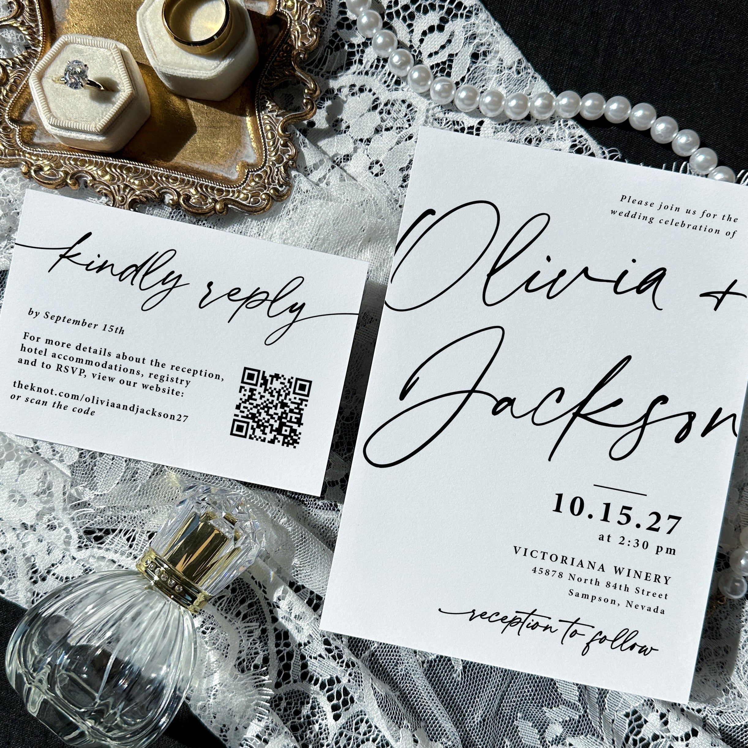 Wedding invitation with RSVP card sitting on top of white lace fabric. Around the wedding suite are a perfume bottle, pearl necklace, and a tray with rings.