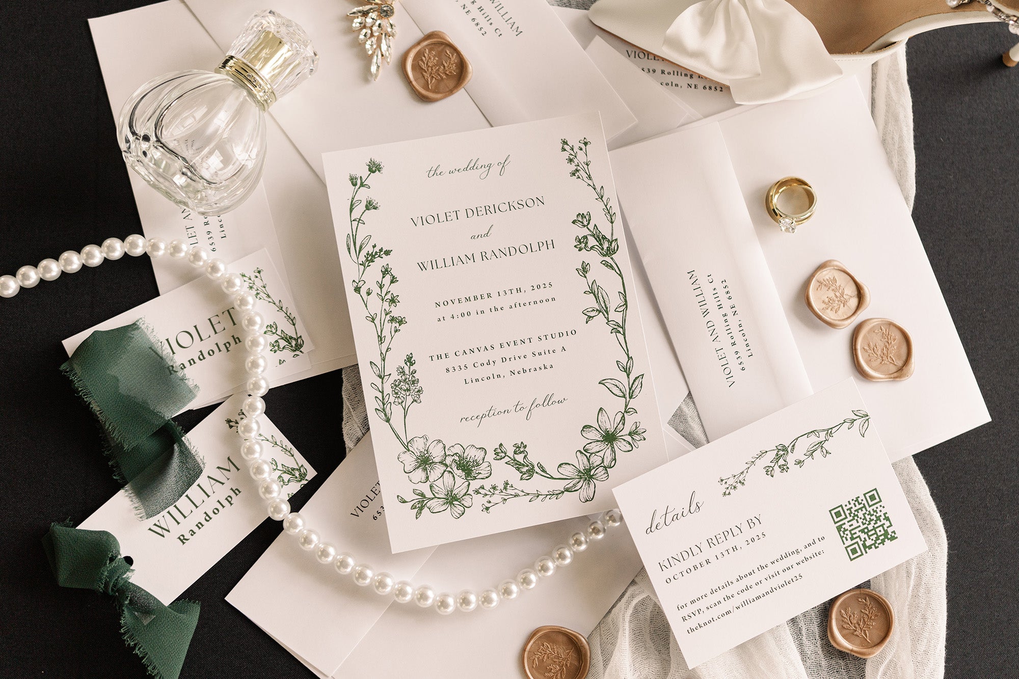 Wedding invitation set with greenery design. The suite is sitting on top of scattered envelopes with various accessories arranged around them.
