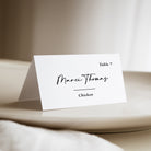 Modern black and white place card staged on a plate against a beige background.