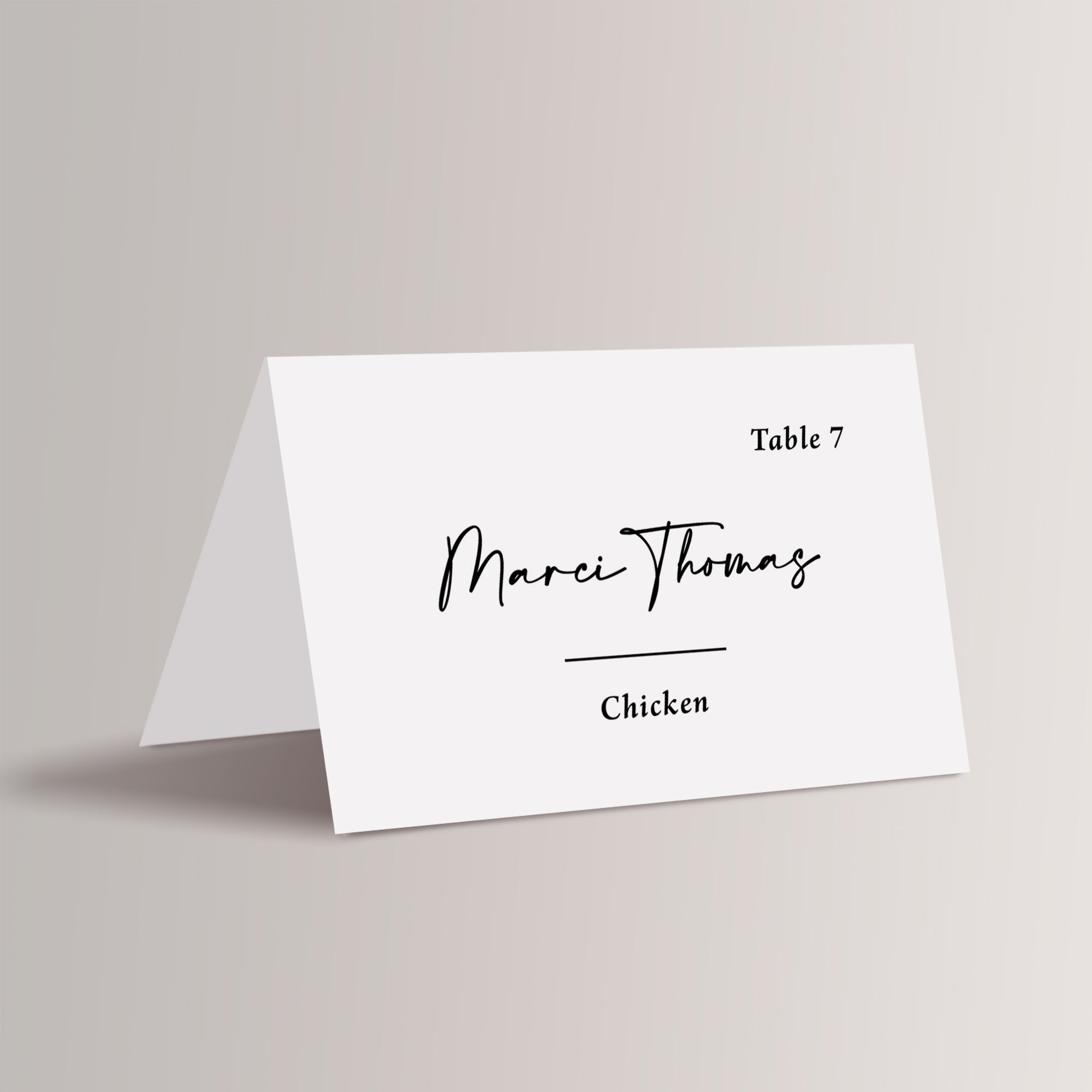 Black and White Place Card staged against a plain beige background. In the center of the place card is the guest name in a large script font, below that is a horizontal line, with the meal choice in an italic serif font below that. A table number is in the upper right corner in also in an italic serif.